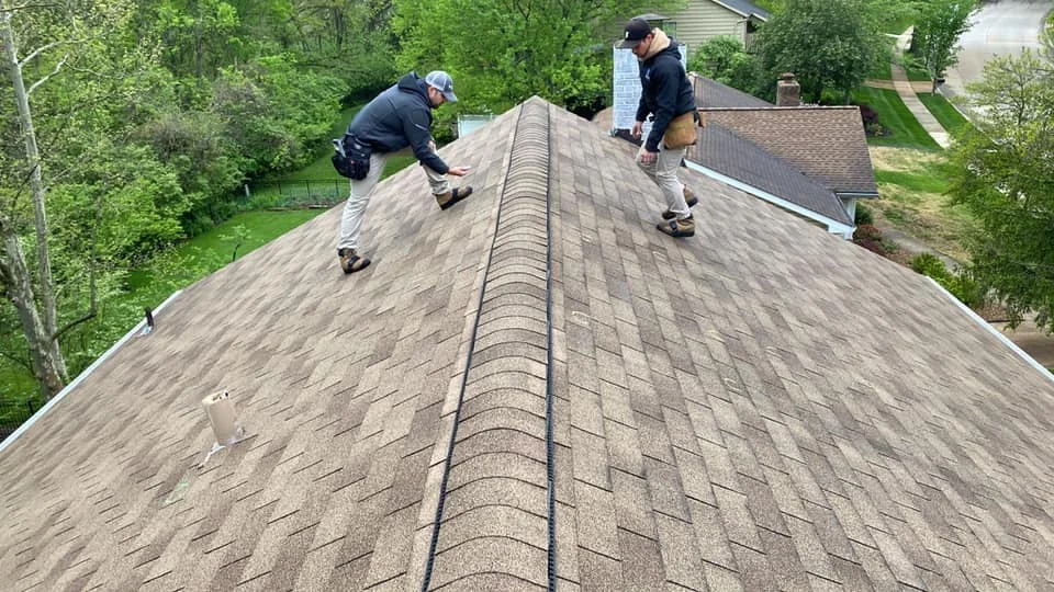 Two people examining asphalt shingles during an on-roof inspection