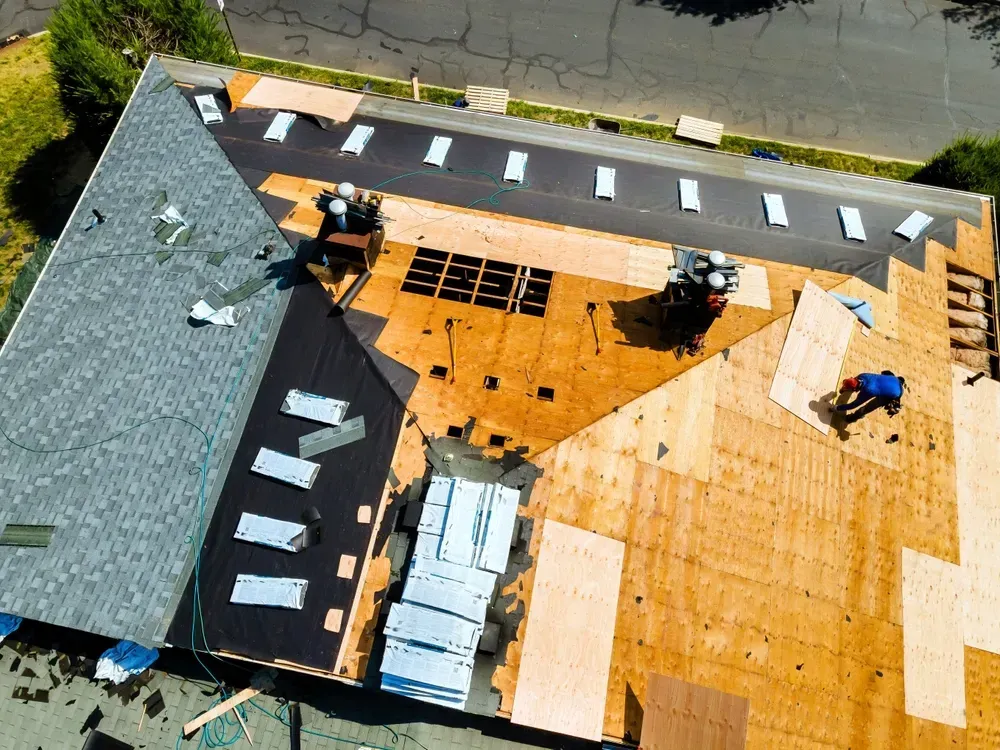 Roof replacement in progress with decking, underlayment, and shingle bundles visible